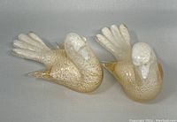 Pair of white glass bird figurines with gold flecks, raised wings, viewed from above showing detailed bird shapes