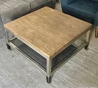 Front angle of the square coffee table showing wooden top, beveled glass shelf, and metal base with rust spots