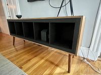 Side front view showing the open cubby compartments of the console table with wood surround and legs on hardwood floor.