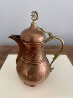 Frontal and side perspective of antique copper Turkish teapot showing detailed hand engravings and crescent moon brass finial