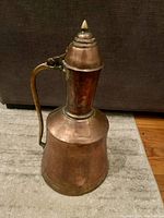 Side view of copper and brass watering jug showing handle and conical lid with finial.