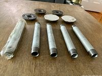 Five galvanized steel pipes and five flanges arranged on a wooden surface. One pipe wrapped, others visible with threaded ends. Flanges circular with bolt holes.