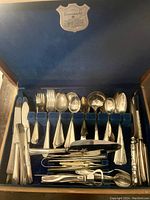 Top view of the silver plated utensils arranged neatly in the blue velvet lined box showing a variety of forks, spoons, knives, and tools with different handle designs.