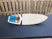 Top view showing white skateboard deck with colorful tail design, textured grip surface, and signs of wear.