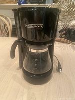 Front view of Black & Decker coffee maker showing the brand logo, glass carafe, and black plastic body.