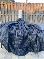 Black pool debris cover loosely gathered and displayed on a table with a wooden fence background.