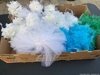 Photo showing white feather boas and white flower garlands with tulle in a cardboard box outdoors.