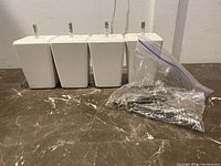 Four small white tapered bed posts aligned in a row with bag of metal screws in front on a brown marbled surface against a white wall.