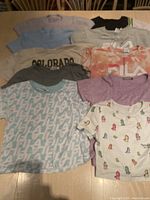Nine girls crop tops in various colors and prints laid out on table