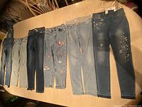 All eight pairs of girls Justice jeans laid out side by side showing various denim washes and decoration details.