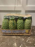 Front view of the set showing four pineapple-shaped bowling pins packaged in a box with plastic wrap.