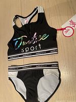 Photo of Justice girls 2 piece swimsuit top and bottom, showing front of top with logo and zipper, and bottoms with waistband branding.