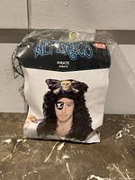 Front view of packaged pirate wig with brand label and model image showing wig and hat with skull graphic, includes model with eyepatch not included in sale.