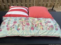 Four patio pillows on a black bench in front of a wooden fence, showing different colorful patterns including solid colors, stripes, and tropical prints.