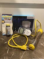 Photo showing Intex pool heater with yellow power cord, digital water tester, and AquaChek pool and spa test strips in package