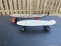 Both skateboards placed side by side, visible deck graphics on one and white plastic texture on the other.