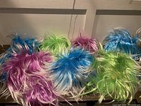 Photo shows six synthetic wigs in bright colors laid out on a flat surface with white background. Colors include blue, green, purple, and mixed shades. Wigs are short to medium length with some fiber fraying indicating slight wear.