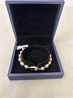 Bracelet inside blue jewelry box on black holder, showing pearl strand and clasp.
