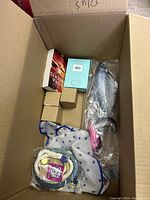 Box with a catfish-shaped plush toy, small cardboard boxes, Belvita product, blue scarf with paw prints, and nautical themed rope bracelet.