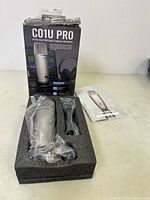 Microphone in foam packaging with plastic wrapping, shock mount, and manual visible, box in background