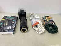 Four items displayed on flat surface: Pelican Marine phone pouch in box, black flashlight, white and green extension cords.