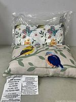 Two lumbar pillows stacked, showing bird printed designs on each side with tags indicating material info.