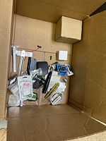 Cardboard box with assorted small packaged and loose miscellaneous household and auto parts including batteries, clips, adapters, and hooks.