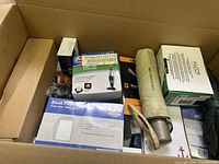Top view of a large cardboard box with various packaged items including a vacuum filter replacement, a metal flashlight with a beige cover, and several boxes and plastic wrapped small items.