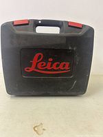 Black hard plastic Leica carrying case with red clasps and Leica logo.