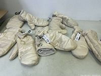 Five pairs of light beige Reitman's winter mittens with tags and adjustable wrist toggles displayed on a flat surface.