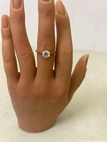 Ring worn on hand showing full ring and main round stone with smaller stones in band.