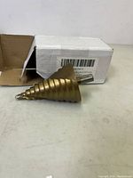 Single large spiral groove step drill bit, titanium coated, shown with packaging box in background.