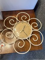 Decorative white wall clock with curly metal frame and cream colored face