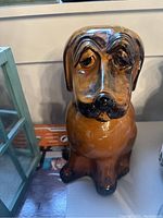 Brown ceramic dog-shaped cookie jar with expressive sad eyes and detailed features, shown from front angle on a shelf.