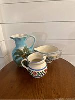 Front view of three pitchers/vases showing varying sizes and designs on a wooden surface.