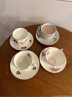 Four different porcelain tea cups with matching saucers on a wooden surface, one cup contains a candle.