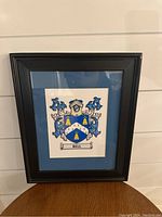 Black frame with blue mat and heraldic design inside, approx 17.5 x 14.5 inches