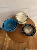 Photo showing all nine mixing bowls grouped together on a round wooden table, includes ceramic, plastic, and black-rimmed bowls