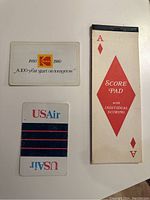Two US Air branded playing cards and a 100 year start on tomorrow advertising card next to Ace of Diamonds Score Pad