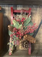 Frontal view of small red wooden sleigh with attached artificial holiday greenery including pinecones and red berries