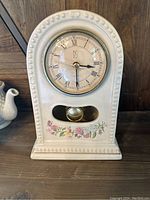 Front view of ceramic clock showing clock face with PS initials, Roman numerals, and floral decoration at base.