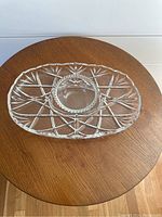 Clear crystal oval plate with intricate geometric cut detailing with a matching small crystal bowl centered on it on wooden surface.