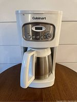 Front view of white Cuisinart coffee maker showing control panel with four buttons and digital display, and stainless steel carafe with white handle.