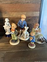 Image of five figurines including children and animals in various poses on a wooden surface.