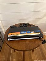 Front top view of Samsung HD DVD Player showing HDMI and HD capabilities stickers, alongside remote and cables on round wooden table.