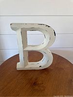 Front-side view of solid wood letter B showing distressed white paint and black accent marks.