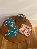 Set of four trivets: two cat-shaped ceramic trivets, one black metal trivet, one square mosaic tile trivet on round wooden table.
