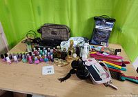 Photo showing full lot of 12 assorted beauty products including nail polishes, hair care kits, combs, clips, wallet and perfumes on wooden table with green background.