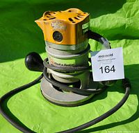 Black & Decker router model 7616-04 showing orange top and grey base with a power cord wrapped around it, visible branding, placed on green background.