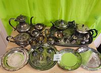 Full lot view showing all silver plated items including tray, tea pots, wine goblets, salt & pepper shakers and candle holders.